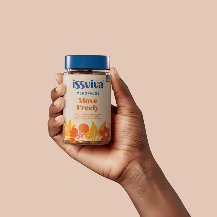 Hand holding a bottle of issviva Menopause Move Freely supplement against a beige background