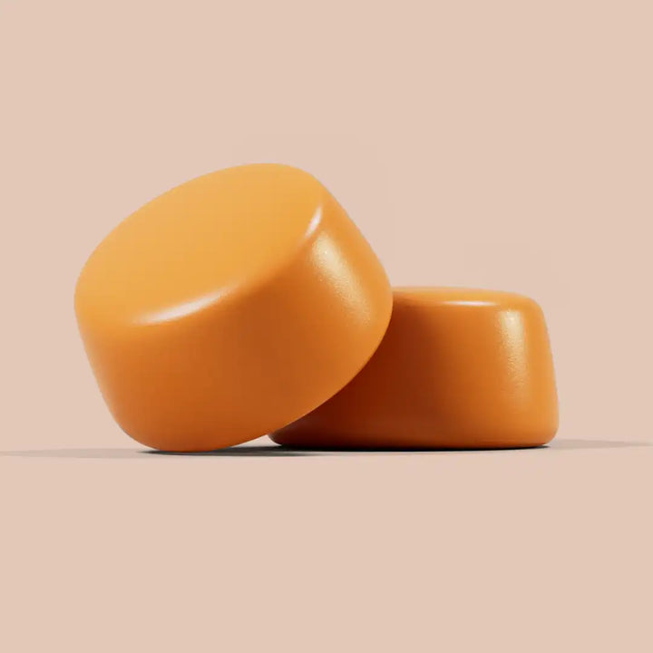Two orange cylindrical gummies on a beige background