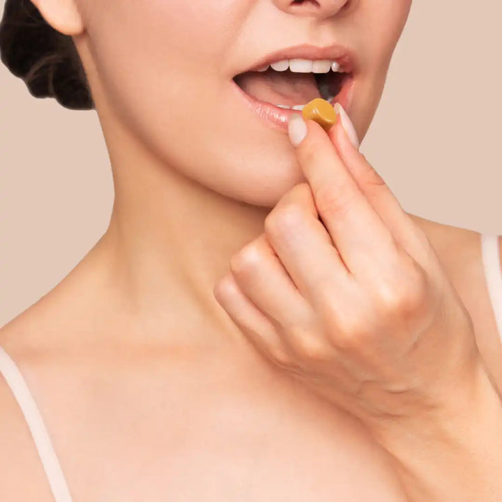 Woman applying a small gummies to her lips against a beige background
